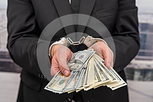 young male businessman in a classic suit and tie holds his hands in handcuffs.