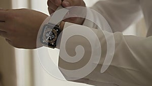 Young male businessman puts on a smart watch on his hand while standing by the window