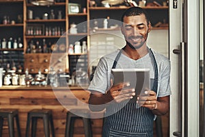 Young male cafe owner looking at digital tablet
