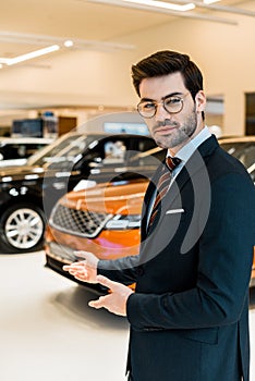 young male car dealer in eyeglasses pointing by hands
