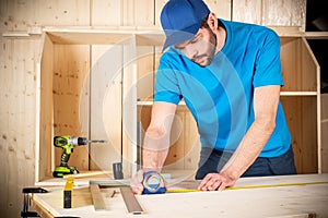 Young male carpenter with beard and metal tape measure at work. measuring wood plank  woodworking construction tool concept