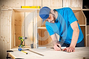 Young male carpenter with beard pencil and stop angle meter at work. measuring wood plank  woodworking construction tool concept