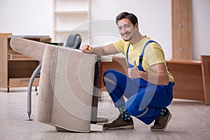 Young male carpenter repairing arm-chair in the office