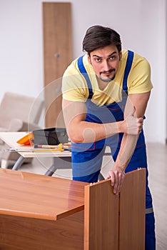 Young male carpenter repairing desk in the office