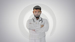 Young male caucasian doctor standing with folded hands on gradient background.