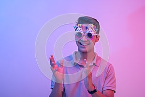 A young male celebrant clapping or giving applause. Wearing hilarious birthday novelty shades and having a good time. Lit with