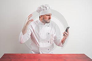 Young male chef in white uniform holding smartphone, texting, looking nervously
