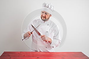 Young male chef in white uniform sharpen the knife blade