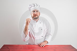 Young male chef in white uniform showing fist