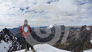 Young male climber standing on the summit of snowy mountain wearing helmet, headlamp, red coat and rope