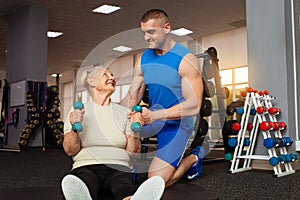young male coach helps an old woman exercise in the gym. Active, sporty, healthy lifestyle. Senior concept. Indoor