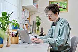 Young male college student sitting at desk at home using laptop