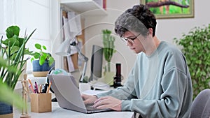 Young male college student sitting at desk at home using laptop