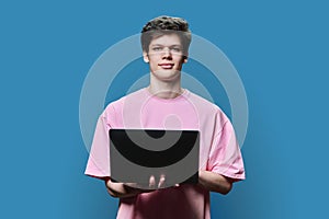 Young male college student using laptop, blue background