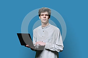 Young male college student using laptop, blue background