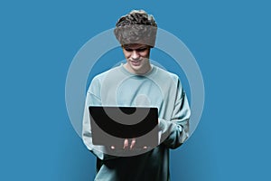 Young male college student using laptop, blue studio background