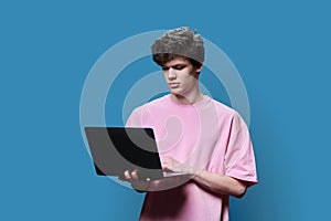 Young male college student using laptop, blue studio background