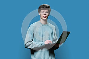 Young male college student using laptop, blue studio background