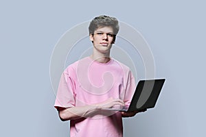 Young male college student using laptop, grey background