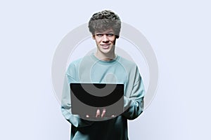 Young male college student using laptop, white studio background