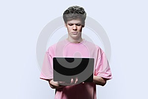 Young male college student using laptop, white studio background