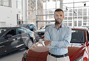 Young male consultant in auto show standing near cars and looking at camera