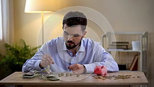 Young male counting coins, piggy bank standing by, financial literacy, budget