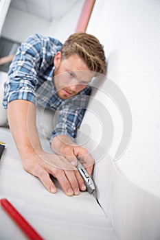 Young male craftsman fitting carpet on floor