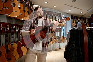 Young male customer choosing acoustic guitar at shop touching neck of instrument