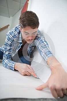 Young male cutting carpet with blade