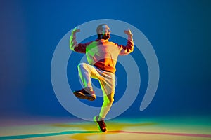 Young male dancer dancing hip-hop isolated over blue background in neon light