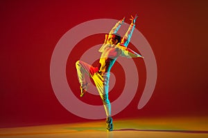 Young male dancer dancing hip-hop isolated over red background in neon light