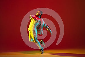 Young male dancer dancing hip-hop isolated over on red background in neon light