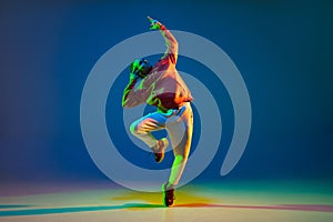 Young male dancer posing isolated over blue background in neon light