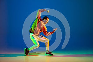 Young male dancer posing isolated over blue background in neon light