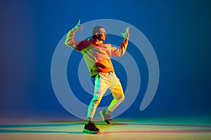 Young male dancer posing isolated over blue background in neon light