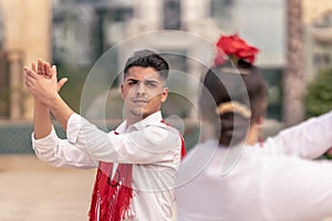 young male dancer in a red mantillo clapping his hands while dancing flamenco with his partner in the street photo