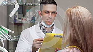 Young male dentist talking to his female patient, examining medical papers