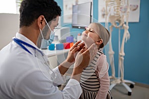 Young male doctor checking little girl's lymph nodes in his office.