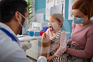 Young male doctor checking little girl's throat in his office.