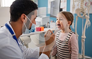 Young male doctor checking little girl's throat in his office.