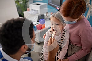 Young male doctor checking little girl's throat in his office.