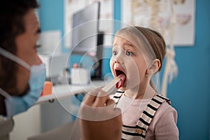 Young male doctor checking little girl's throat in his office.