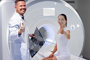 Young male doctor and female patient hold thumbs up in MRI room