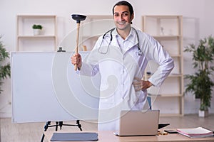 Young male doctor holding plunger in funny concept