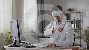 Young male doctor holding a video conference while sitting in the office in vk glasses