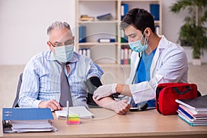 Young male doctor visiting old businessman at workplace