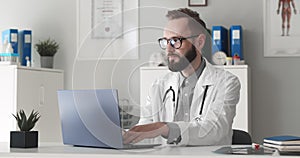 Young male doctor working on laptop in clinic office