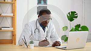 Young male doctor is writing during online consultation at table in modern clinic spbas.