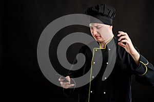 Young male dressed in a black chef suit reading and sending text messages on cellphone looking nervously